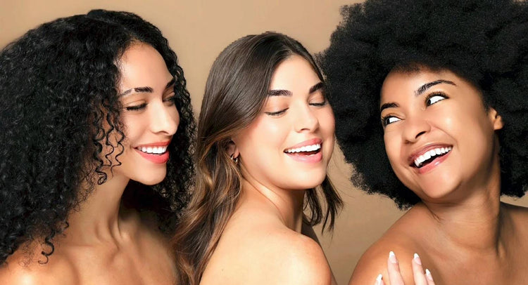 Three women with different hair types smiling against a beige background