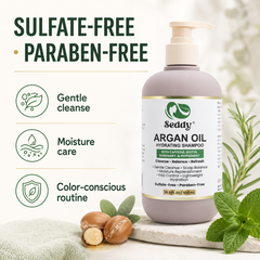 A bottle of Seddy Argan Oil Hydrating Shampoo stands on a light surface with mint leaves and argan nuts around it. The bottle is taupe with a cream pump and a white label with green and gold details.